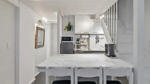 Een moderne keuken met witte kasten, een centraal eiland en een eethoek met een witte tafel en stoelen.