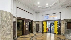 Een hotel lobby met een marmeren vloer, een glazen deuropening en een bordje met 'PB Hotels'.