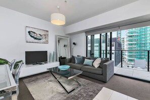 A modern living room with a flat-screen TV, a glass coffee table, and a grey sofa with cushions. - Superb One Bedroom Near Britomart by Zodiak Stays (Auckland)