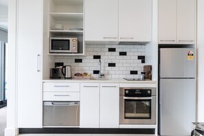 A modern kitchen with white cabinets, a microwave, a coffee maker, a kettle, a dishwasher, and a built-in oven.