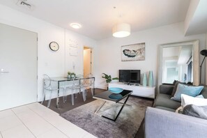 A modern living room with a glass dining table, a sofa, a TV, and a painting on the wall. - Superb One Bedroom Near Britomart by Zodiak Stays (Auckland)