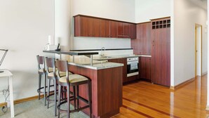 A modern kitchen with wooden cabinets, a central island, bar stools, and a built-in oven. - Relaxing Sea Wharf View Apartment by Zodiak Stays (Auckland)