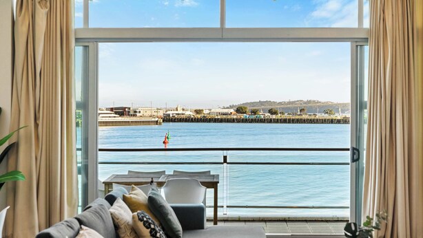 A room with a view of a waterfront, a sofa, a table, and curtains. - Relaxing Sea Wharf View Apartment by Zodiak Stays (Auckland)