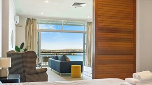 A hotel room with a bed, a sofa, a small table with a lamp, and a view of the sea. - Relaxing Sea Wharf View Apartment by Zodiak Stays (Auckland)
