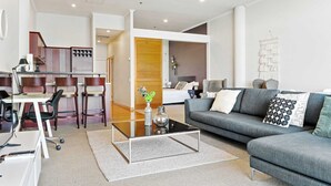 A modern living room with a sofa, coffee table, and dining area. - Relaxing Sea Wharf View Apartment by Zodiak Stays (Auckland)