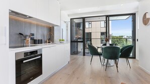 Een moderne keuken met witte kastjes, een ingebouwde oven en een eethoek met groene stoelen en een tafel.