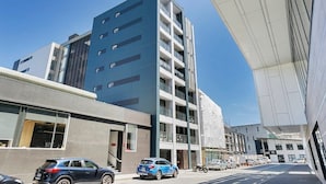 Een modern meerlaags gebouw met een platte gevel, grote ramen en een parkeerplaats met auto's.