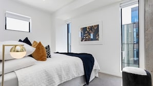 Een moderne slaapkamer met een groot bed, een nachtkastje, een vloerlamp en een raam met uitzicht op de stad.