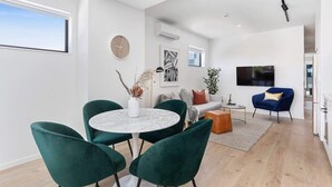 Een moderne woonkamer met een ronde tafel, groene stoelen, een bank en een televisie.