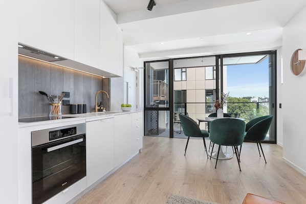 Una cocina moderna con horno empotrado, comedor con mesa y sillas, y balcón con vistas.