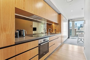 Una cocina moderna con armarios de madera, una campana extractora de acero inoxidable y vistas a la ciudad a través de grandes ventanales.