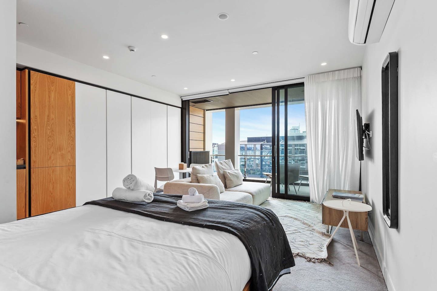 A modern hotel room with a large bed, a seating area with a view, and a balcony.