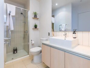 A modern bathroom with a glass-enclosed shower, a toilet, a sink with a mirror, and a small shelf with plants.