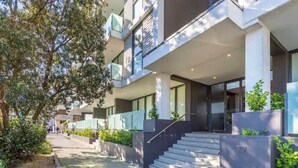 A modern building with a covered entrance, steps leading to the entrance, and a number '77' visible on a wall. - Wynyard Viaduct Harbour 2BR+Parking: Zodiak Stays (Auckland)