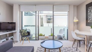 A modern living room with a sofa, a round coffee table, a TV, and a balcony with sliding doors. - Wynyard Viaduct Harbour 2BR+Parking: Zodiak Stays (Auckland)