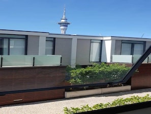Un bâtiment moderne doté de grandes fenêtres, d’une façade en bois et offrant une vue sur une tour en arrière-plan.