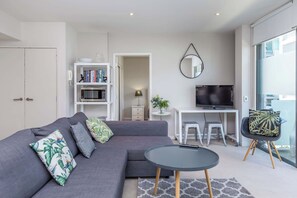 A modern living room with a grey sectional sofa, a glass coffee table, a flat-screen TV, and a bookshelf. - Wynyard Viaduct Harbour 2BR+Parking: Zodiak Stays (Auckland)