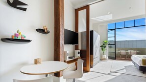 Une chambre d’hôtel moderne avec une table ronde, des chaises blanches, un lit, une télévision et une grande fenêtre.