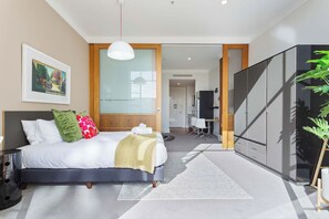 A modern hotel room with a bed, bedside table, and a large wardrobe. - Lovely Bright Apt w/ Pool and Gym by Zodiak Stays (Auckland)
