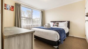 Ein Hotelzimmer mit Bett, Schreibtisch, Fenster mit Vorhängen und einem Wandbild.