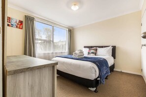 Ein Hotelzimmer mit Bett, Schreibtisch, einem Fenster mit Vorhängen und einem Bild an der Wand.