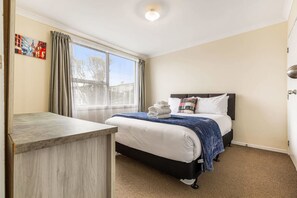 A hotel room with a bed, a desk, and a window with curtains.