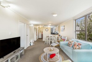 A compact living space with a TV, sofa, and dining area. - Lovely 2-Bedroom Rental with Parking by Zodiak (Auckland)