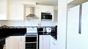 Eine kleine Küche mit weißen Schränken, einem Herd, einer Mikrowelle und einem Kühlschrank.