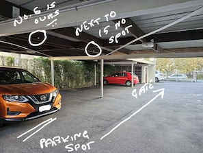 A parking area with a car and a red vehicle, marked parking spots, and a gate.