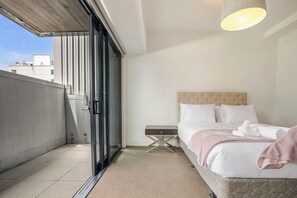 Ein Hotelzimmer mit Bett, Nachttisch, kleinem Tisch und einer Schiebetür zu einem Außenbereich.