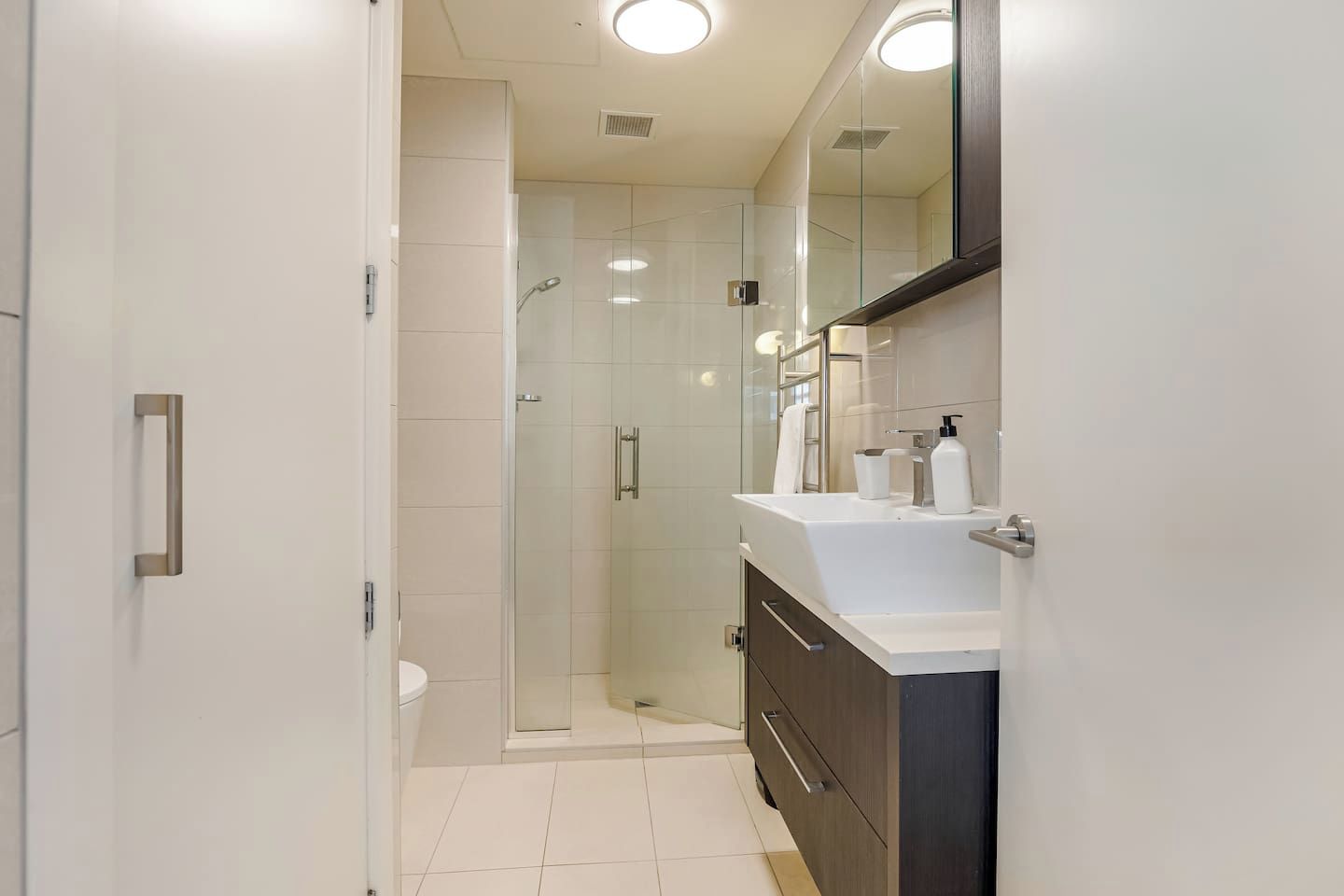 Ein modernes Badezimmer mit einer Duschkabine aus Glas, einem weißen Waschbecken und einem großen Spiegel.