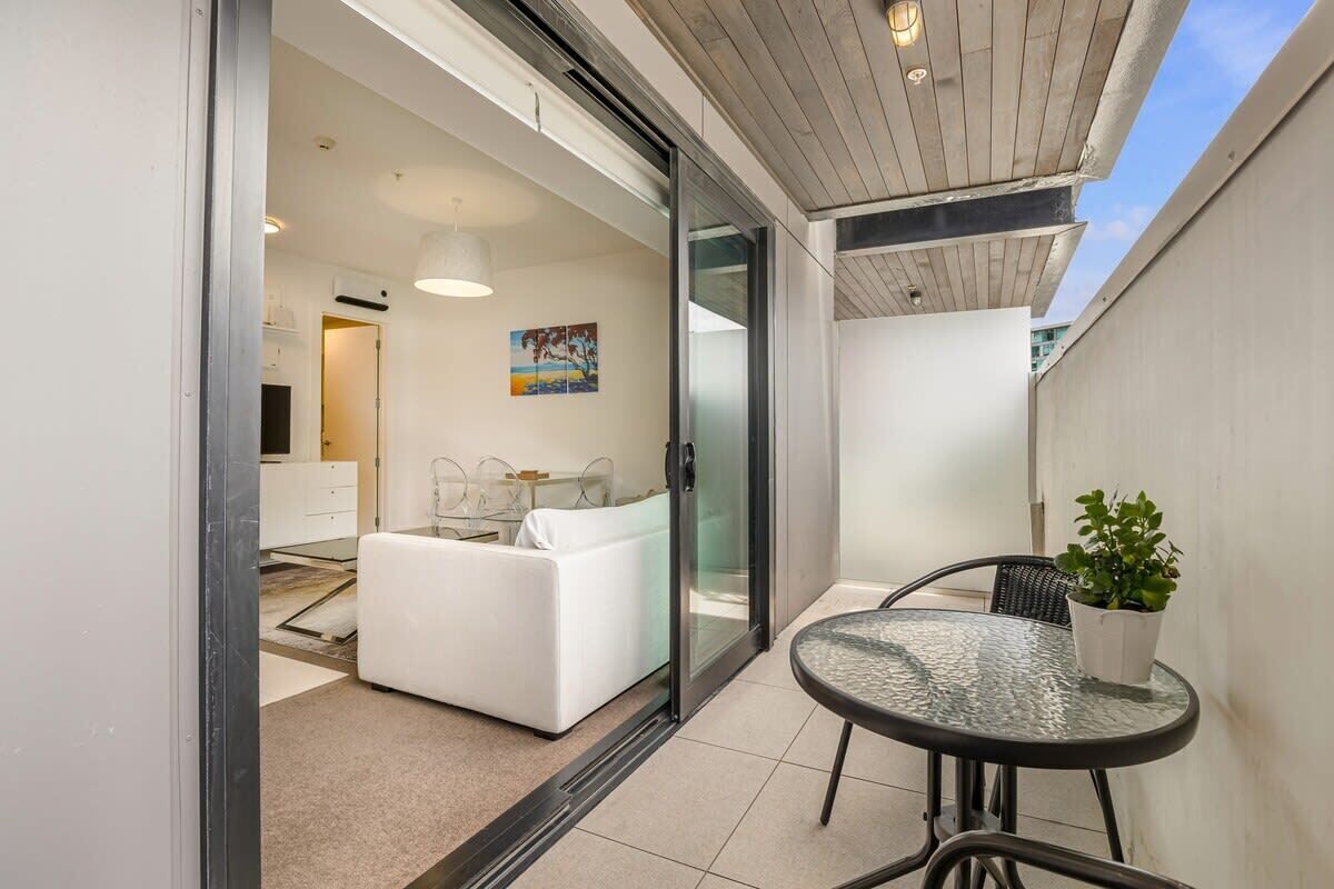A modern interior with a glass door leading to a balcony, a white sofa, a small round table with a potted plant, and a painting on the wall.