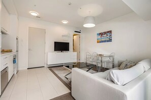 A modern living room with a white sofa, a glass coffee table, and a dining area with clear chairs. - Bright Modern 1BR in Auckland CBD by Zodiak Stays (Auckland)