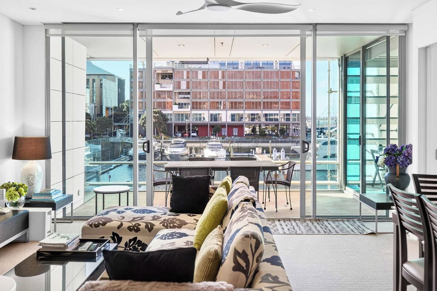 Een moderne woonkamer met een bank, een salontafel en uitzicht op een jachthaven door grote glazen deuren.