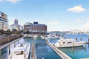 Marina con varios yates amarrados, un edificio moderno con el letrero 'Park Hyatt' y un paseo marítimo.