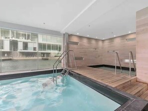 Ein modernes Hallenbad mit großen Glaswänden, Holzboden und Metallgeländern.