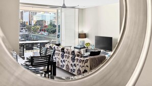 A modern living room with a sofa, a TV, and a dining area with chairs and a table. - Gorgeous 2BR in Wynyard Quarter by Zodiak Stays (Auckland)