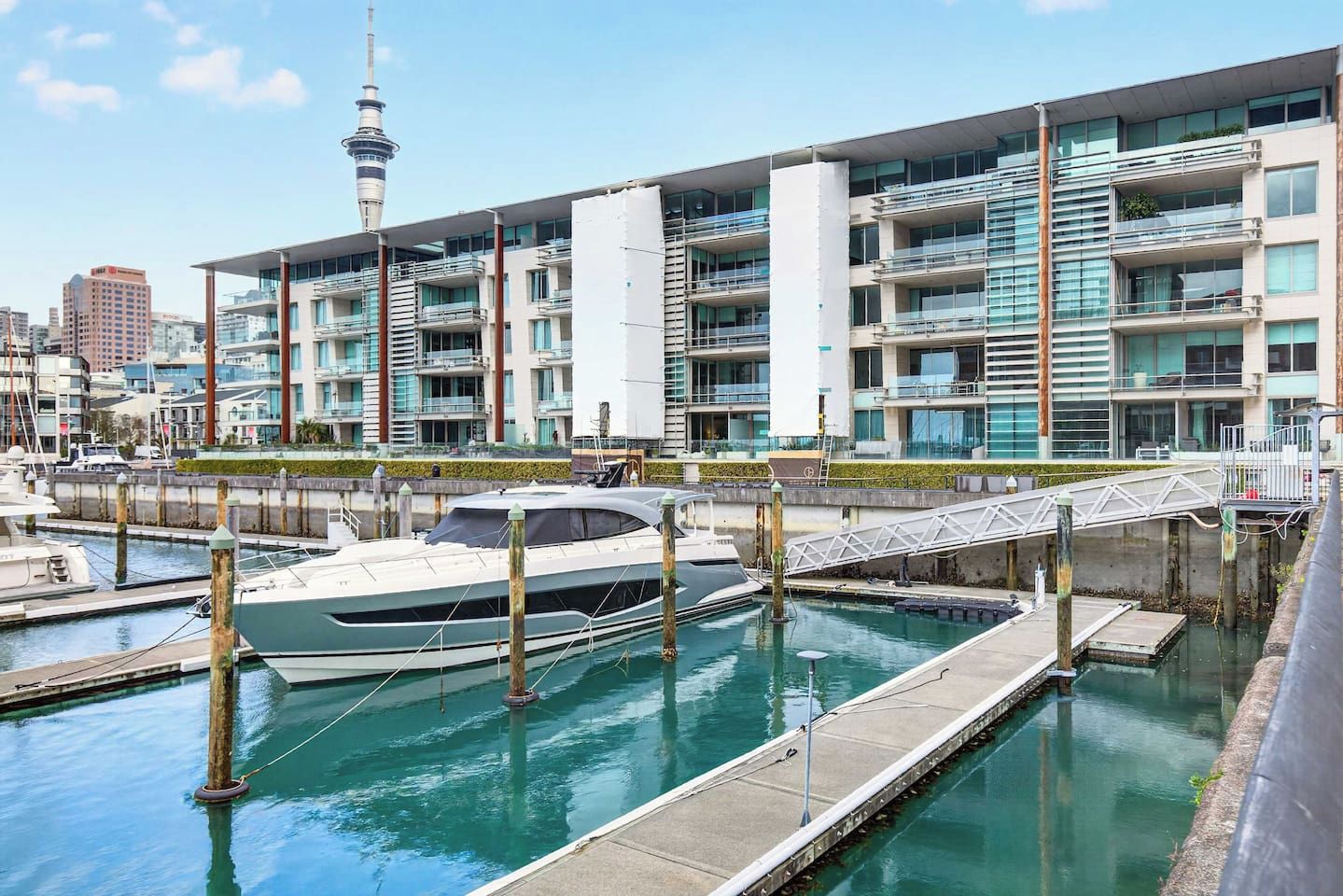 Un port de plaisance avec un yacht amarré, des immeubles modernes dotés de balcons et une tour en arrière-plan.
