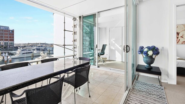 A modern balcony with a glass door leading to a room, a dining table with chairs, and a view of the cityscape. - Gorgeous 2BR in Wynyard Quarter by Zodiak Stays (Auckland)
