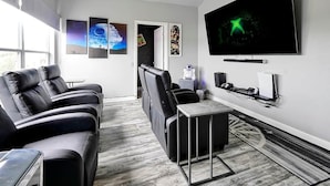 Una sala de estar moderna con un televisor de pantalla plana grande, sofás de cuero negro, una mesa de centro y obras de arte en las paredes.