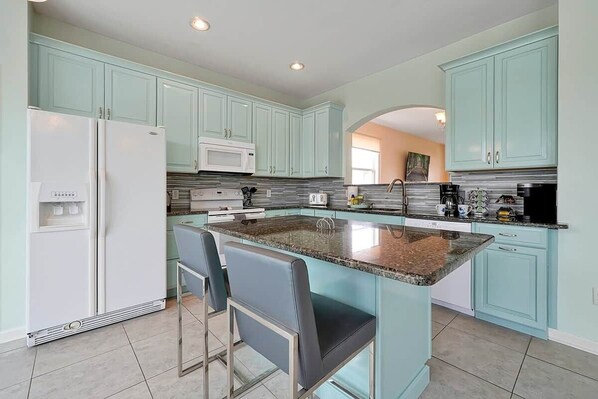 A modern kitchen with teal cabinets, a granite countertop, and stainless steel appliances.