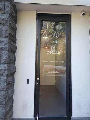 A hotel entrance with a glass door, a stone wall, and a sign indicating it's a guest check-in station.