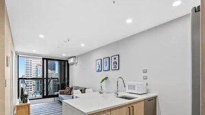 A modern kitchen with a white countertop, wooden cabinets, and a built-in microwave. - Stunning 2BR w/ Views Near Sky Tower- Zodiak Stays (Auckland)