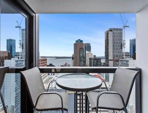Ein Balkon mit Tisch und Stühlen, mit Blick auf eine Skyline und ein Gewässer.