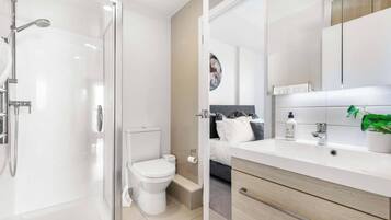 A modern bathroom with a glass shower enclosure, a toilet, and a vanity with a sink and mirror.
