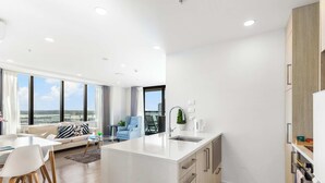 A modern apartment with a kitchen, dining area, and living room with a large window. - Sky Tower Views | 2 Bed 2 Bath CBD | Zodiak Stays (Auckland)