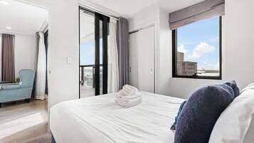 A hotel room with a bed, a chair, a window with a view, and a door leading to an outdoor area.