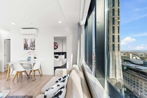 A modern living space with a dining area, a sofa with a view, and a large window overlooking a cityscape. - Sky Tower Views | 2 Bed 2 Bath CBD | Zodiak Stays (Auckland)
