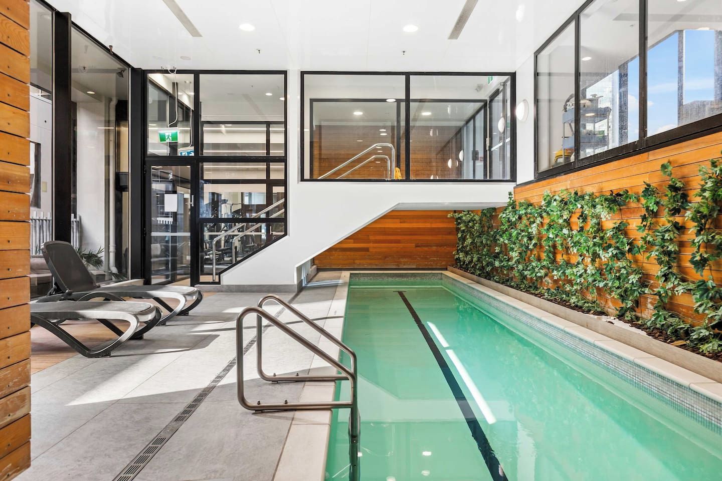 An indoor swimming pool with a wooden wall and a staircase leading to an upper level.