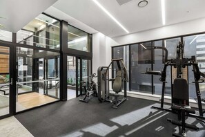 A modern gym with exercise equipment, large windows, and a view of the city. - Sky Tower Views | 2 Bed 2 Bath CBD | Zodiak Stays (Auckland)